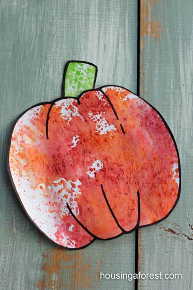 A mottled orange and red Kool-Aid print cut into a pumpkin shape with a green stem, on teal painted boards