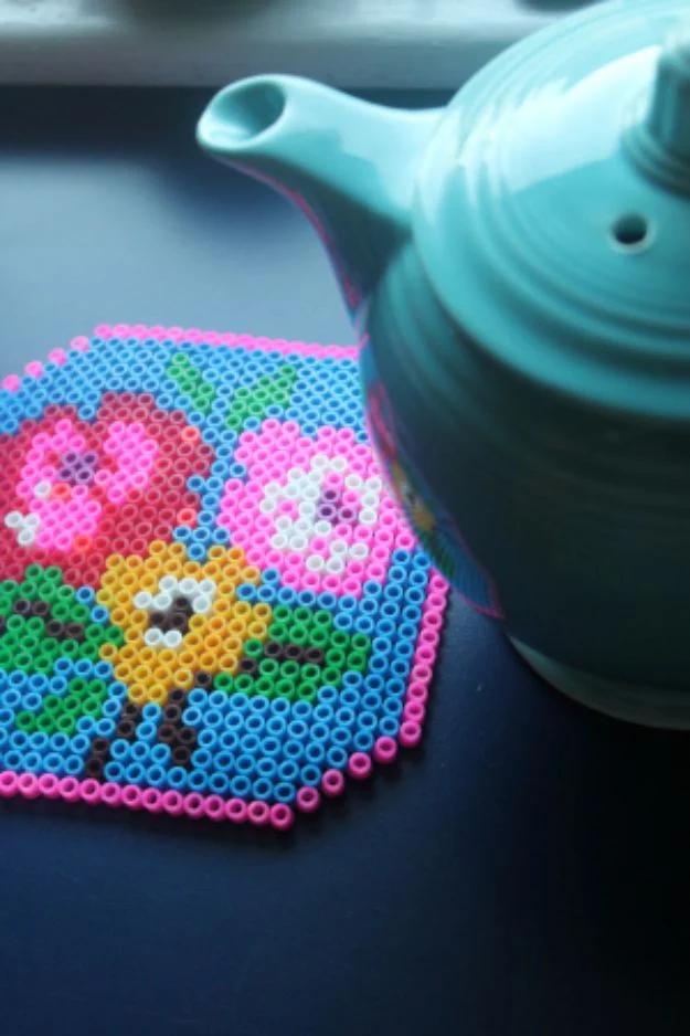 Perler bead trivet, a hexagonal fused bead trivet with a pink and blue floral design beside a teal teapot
