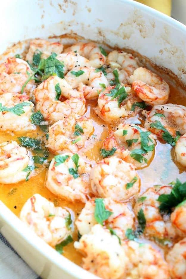 Baked butter garlic shrimp in a dish, pink shrimp sitting in golden garlic butter with chopped parsley