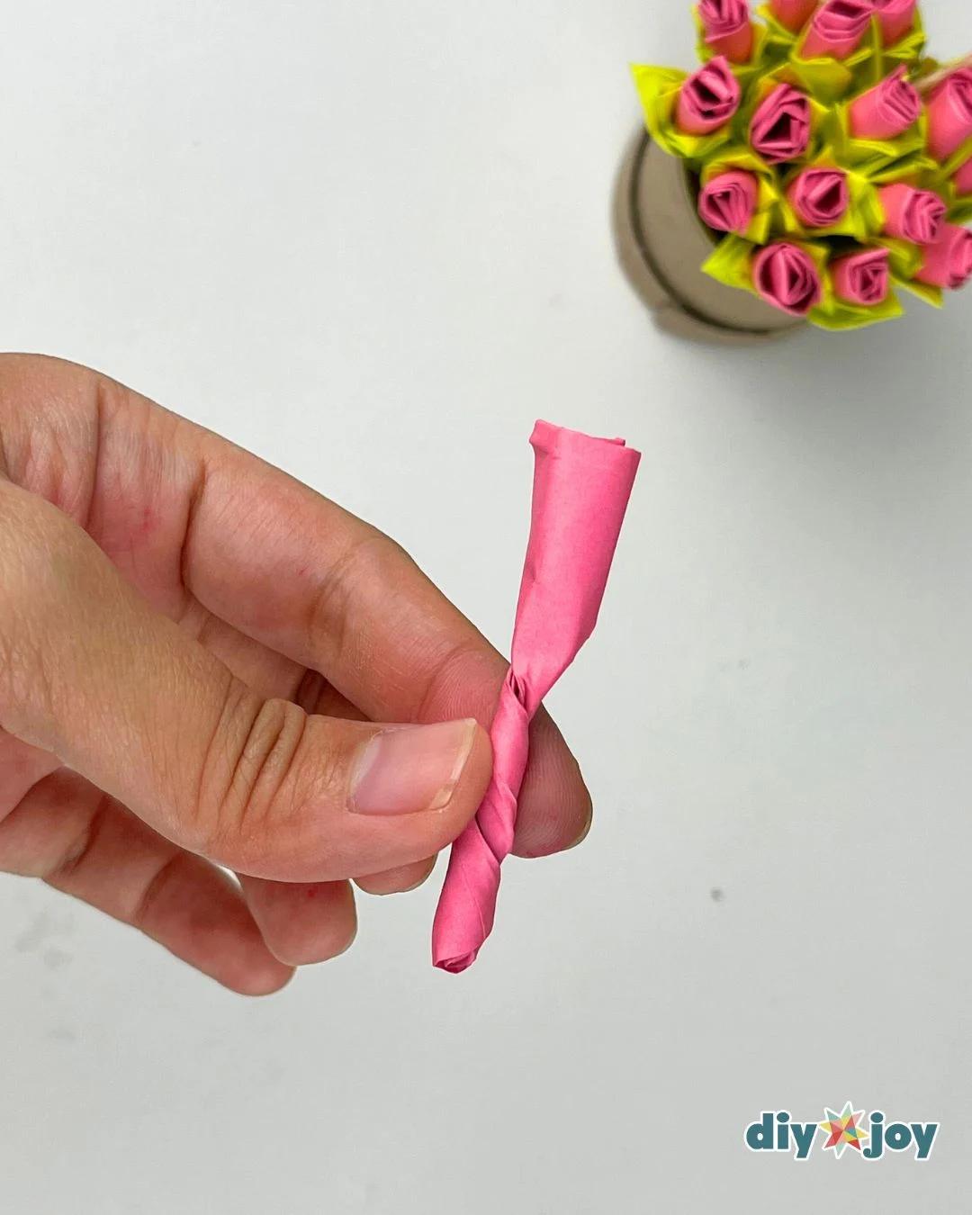 Hand holding a folded pink paper strip cut into a spiral, the first step of a Post-it note paper rose