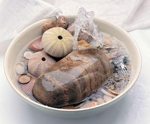 Shallow white bowl fountain holding sea urchin shells, a flat stone and small pebbles with bubbling water
