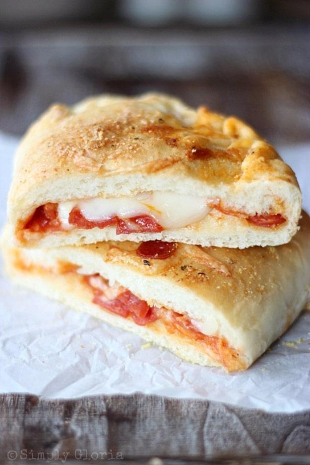 Homemade stuffed pizza pocket cut in half showing pepperoni and melted mozzarella inside golden dough