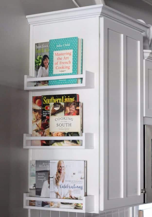 Three narrow white IKEA spice racks mounted in a column on a kitchen cabinet end panel, holding cookbooks face out