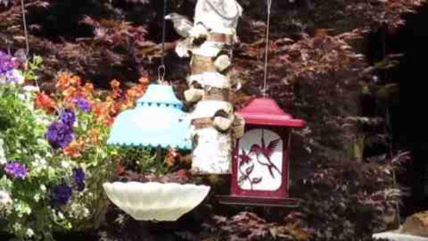 Cluster of upcycled bird feeders on a garden bracket, blue lamp shade feeder, white scalloped dish bath and red lantern