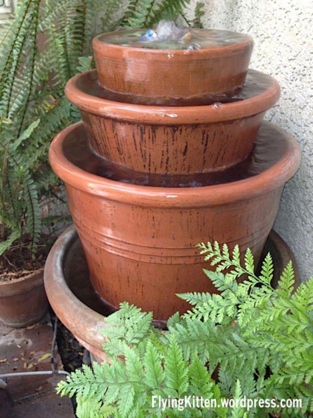 Three stacked terracotta clay pots brimming with water beside garden ferns in an afternoon fountain build