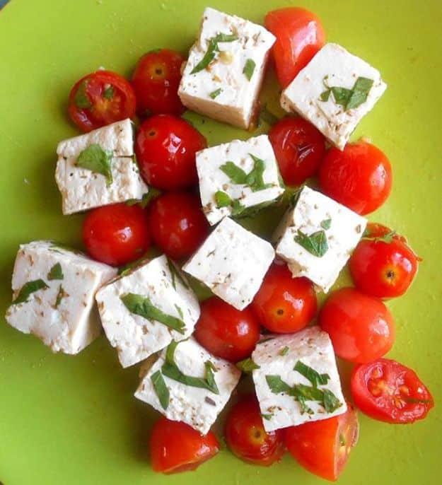 Vegan feta cheese, white marinated tofu cubes with basil and cherry tomatoes on a bright green plate