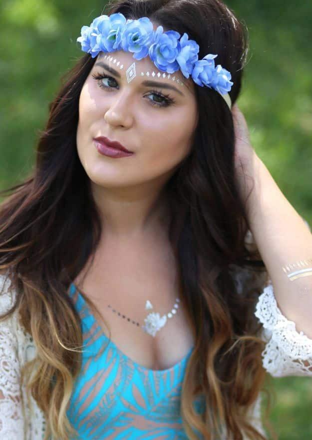 Blue and white faux flower halo crown worn across the forehead by a woman with long dark hair outdoors in green light