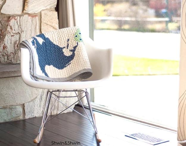 Cream quilt with an appliqued navy world map folded over a white molded chair beside a rough stone wall