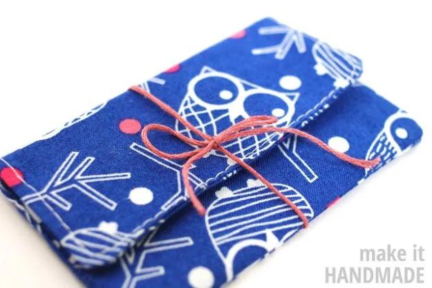 Five minute gift card holder sewn in blue owl print cotton, folded shut and tied with an orange twine bow on a white surface