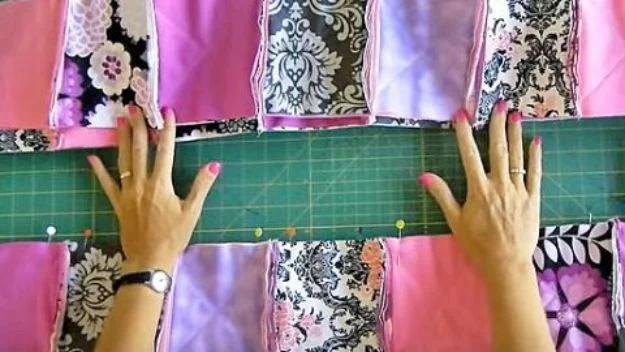 Easy rag quilt in progress, hands aligning pink, purple and black damask fabric strips with pins on a green cutting mat