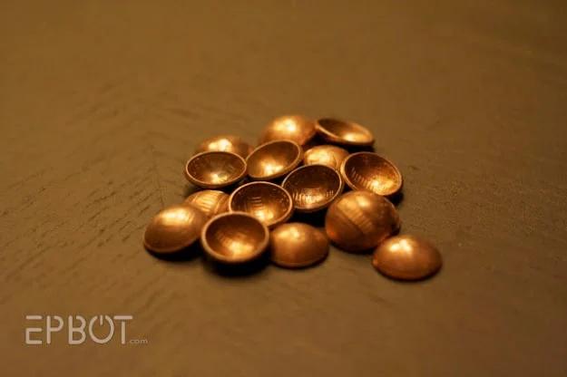 A dozen pennies hammered into shallow copper domes, tipped on their sides on a plain brown background