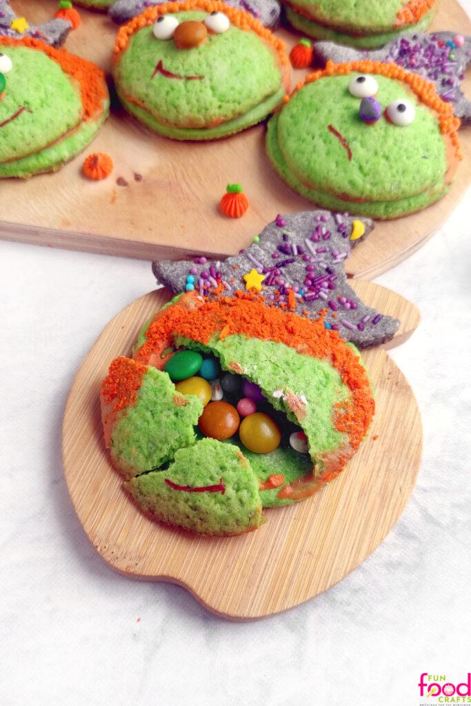 Layered witch piñata cookies with one opened to reveal colorful candy hidden inside on a Halloween serving plate