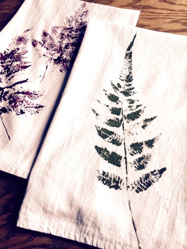 A flour sack tea towel printed with an inked fern in soft green, hanging from an oven handle in a real kitchen