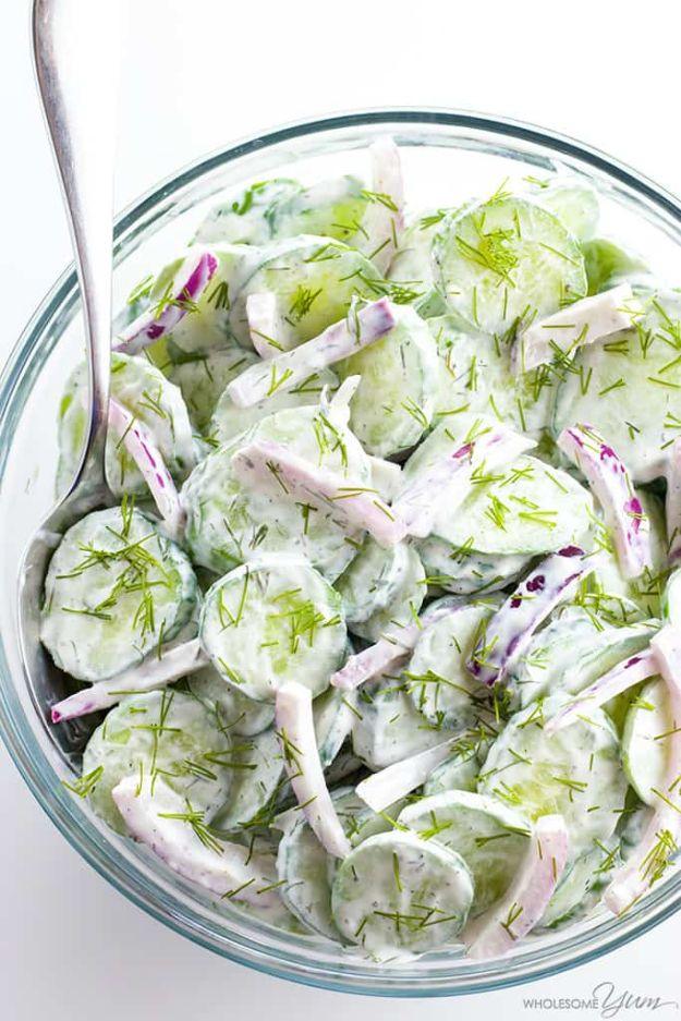 Creamy cucumber salad with red onion slices and fresh dill in a glass bowl with a metal serving spoon
