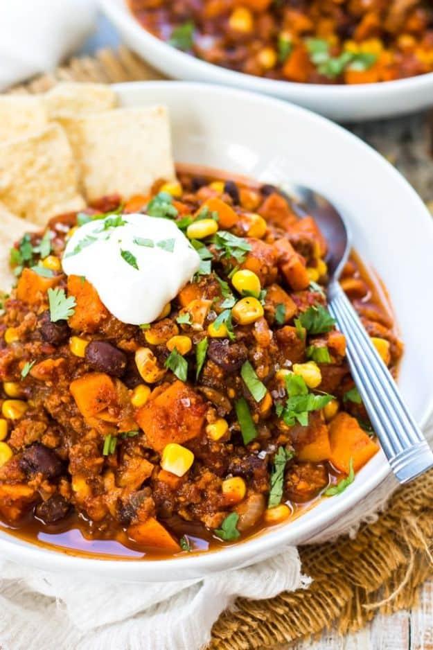 Bowl of sweet potato turkey chili with corn, sour cream and cilantro beside tortilla chips on a woven mat