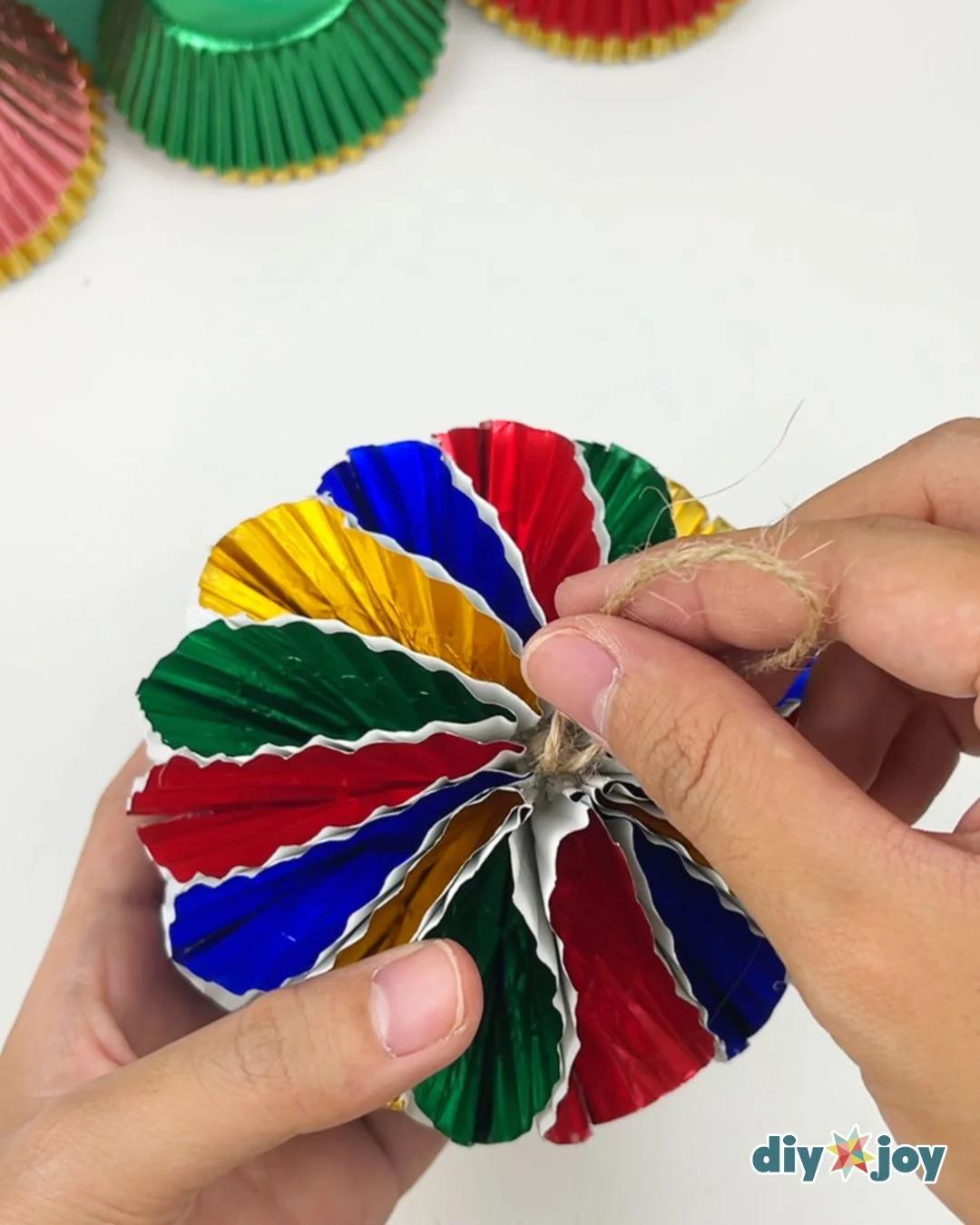 Best DIY Ornaments - hands tucking a loop of jute twine into the center of a fanned out cupcake liner ornament