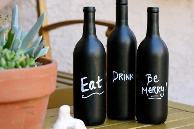 Chalkboard paint wine bottles, three matte black bottles hand lettered eat, drink and be merry by a plant