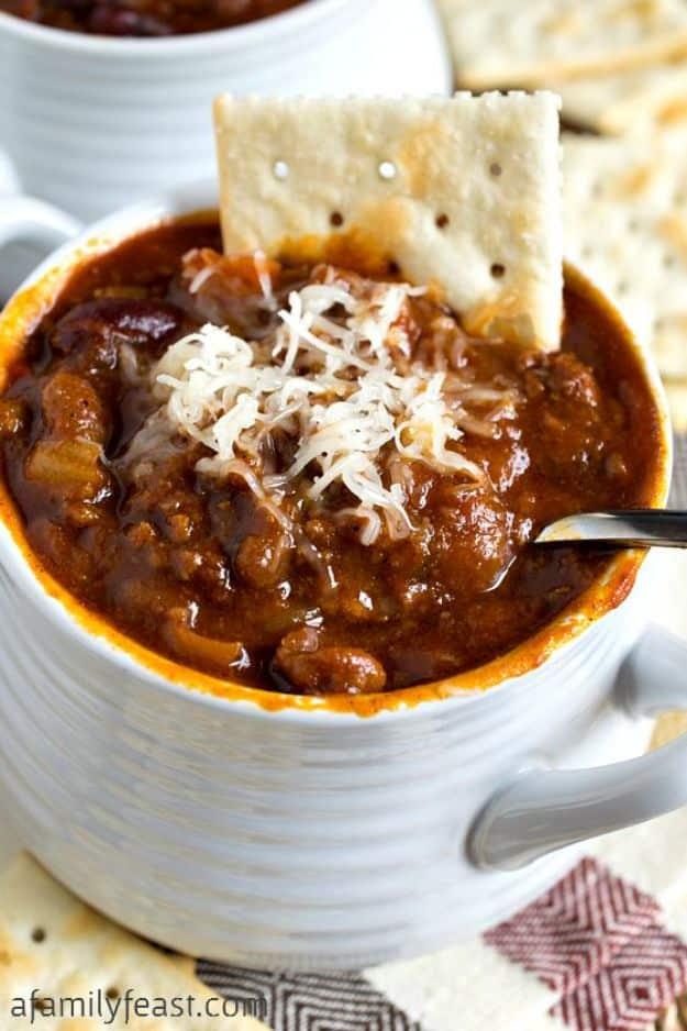 Sweet and spicy slow cooker chili in a white ribbed mug under white shredded cheese with a saltine cracker