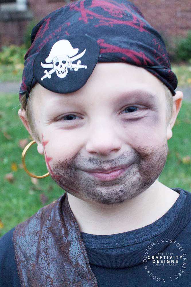 DIY pirate Halloween makeup on a child with a painted beard and mustache, a cheek scar and a black eye patch