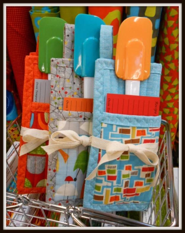 Three folded pot holders holding green, teal and orange silicone spatulas, tied with ribbon in a wire basket