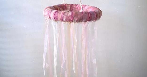 Pink ribbon chandelier with a wrapped ring and long hanging streamers mounted against a plain white wall