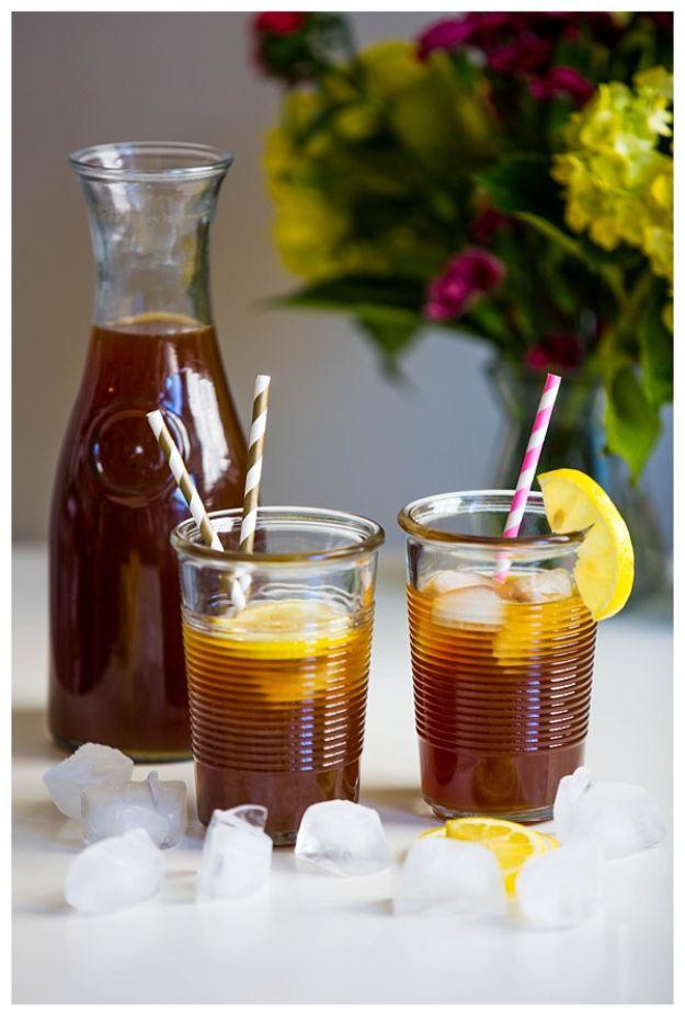 Iced coffee lemonade in two short ribbed tumblers with paper straws and lemon, a cold brew carafe behind