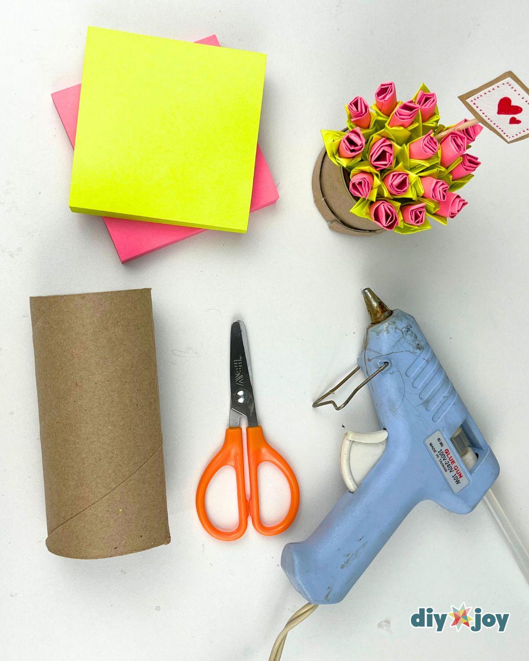 Overhead flat lay of yellow and pink sticky note pads, scissors and glue for a Post-it paper flower craft