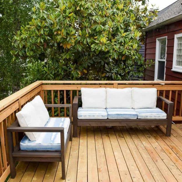 DIY outdoor loveseat and sofa in dark stained cedar with pale striped cushions on a new wooden deck by a red house