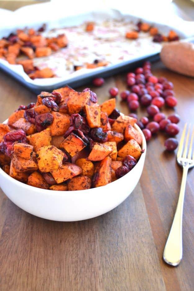 Cinnamon roasted sweet potatoes and cranberries on a parchment lined pan, the berries burst and glossy