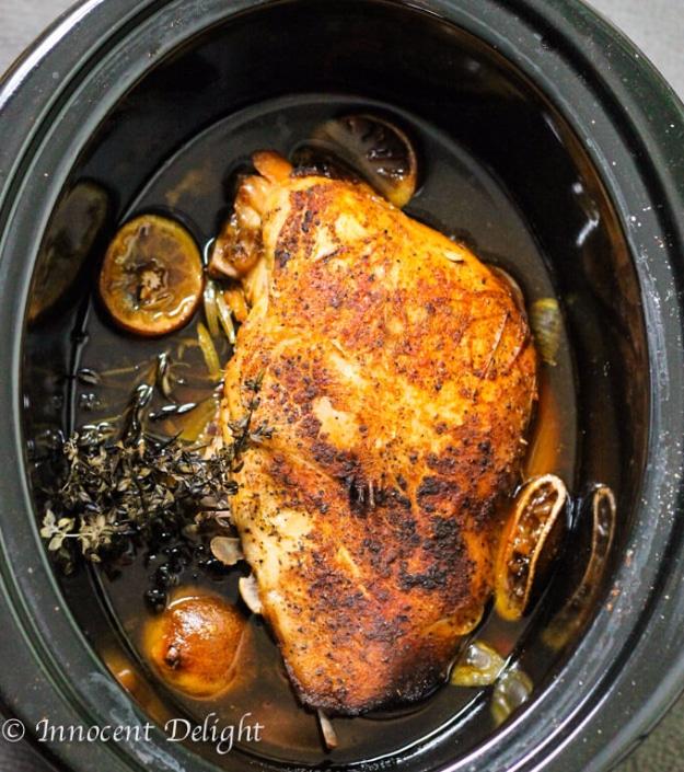Whole browned slow cooker turkey breast with lemon halves, onions and fresh herbs inside a black crockpot