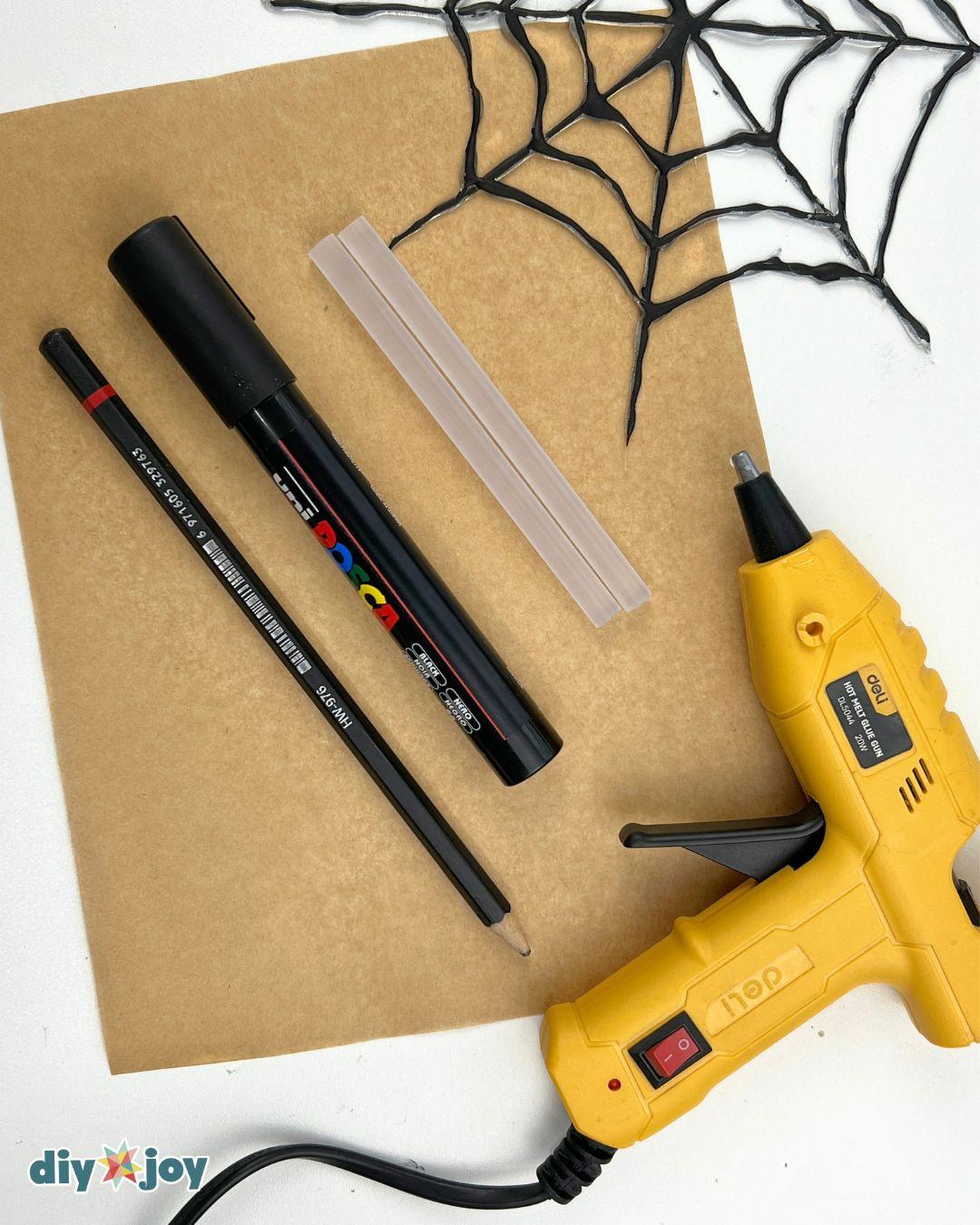 Hot Glue Crafts - a black marker, glue stick and glue gun on kraft paper with a finished spider web in the corner