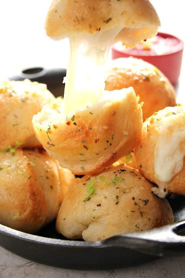 Easy garlic cheese bombs in a black skillet, golden biscuit rolls pulled apart with a long cheese stretch