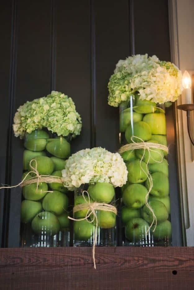 Glass cylinder vases packed with green apples and topped with white hydrangeas tied with twine on a wooden table