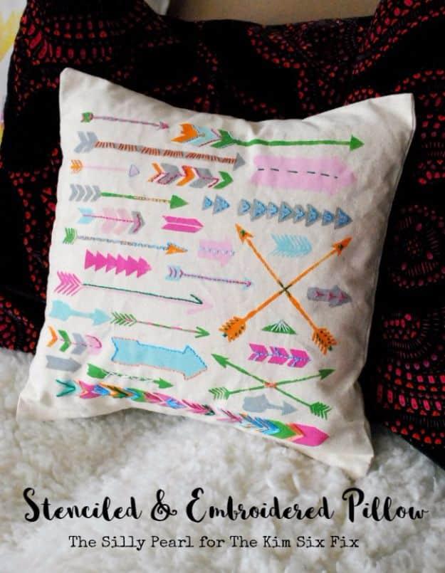 Stenciled and embroidered pillow graphic with multicolor arrows on a cream cover over a dark red throw