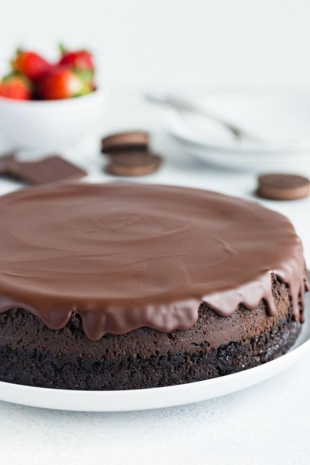 Triple chocolate cheesecake whole on a white plate with a glossy poured glaze over a dark Oreo cookie crust
