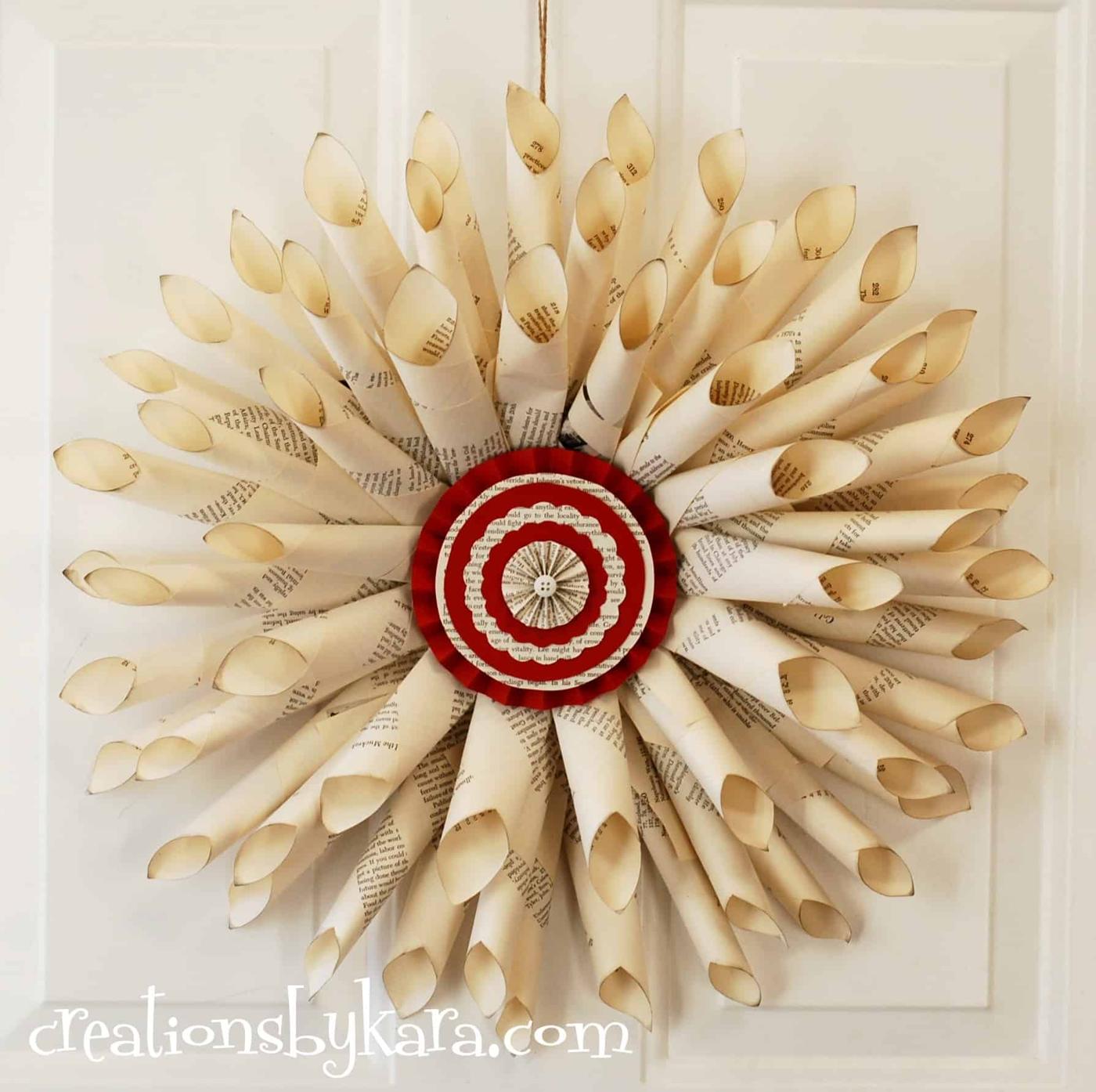 A sunburst wreath of rolled book page cones hanging on a white door with a red and cream layered paper rosette center