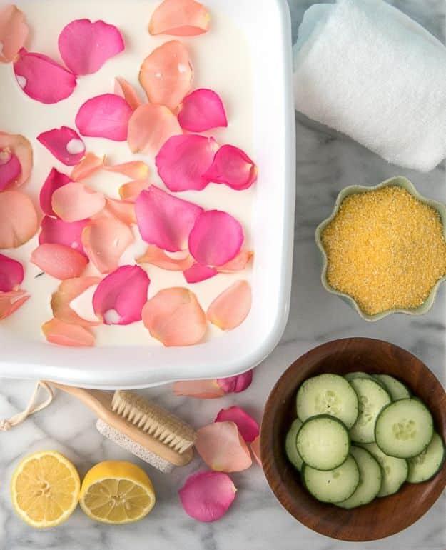 DIY home spa treatment flat lay, a white tray of water and rose petals with cucumber slices, lemons and a nail brush