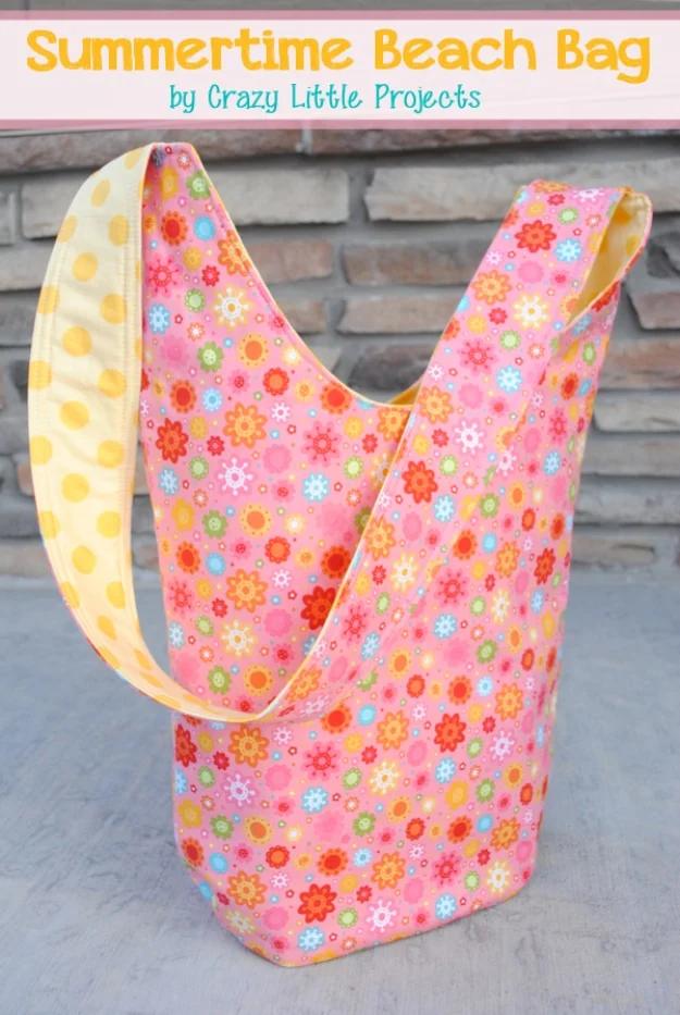 A large striped canvas beach tote with webbing handles, standing on sand with a towel folded inside.