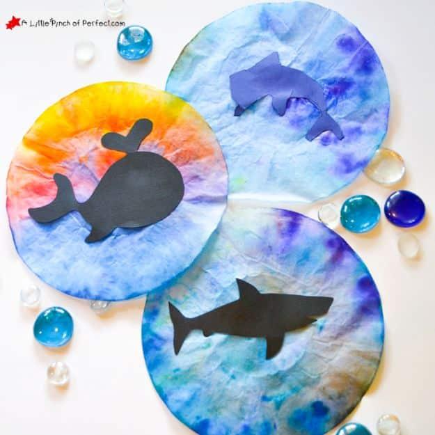 Three coffee filter suncatchers painted in blue, purple and rainbow watercolor with black paper whale, dolphin and shark