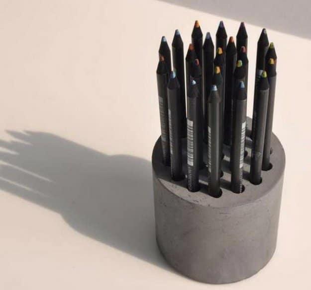 DIY concrete pencil holder, a squat gray cast cement cylinder packed with black pencils casting a long shadow