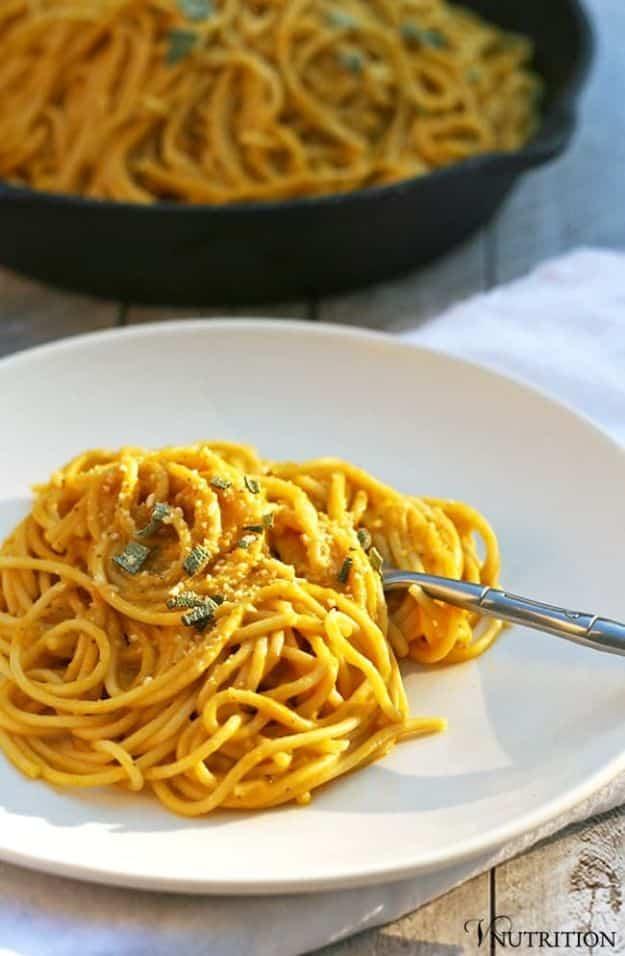 Rich creamy vegan pumpkin pasta on a white plate, golden orange spaghetti twirled with herbs and a skillet behind