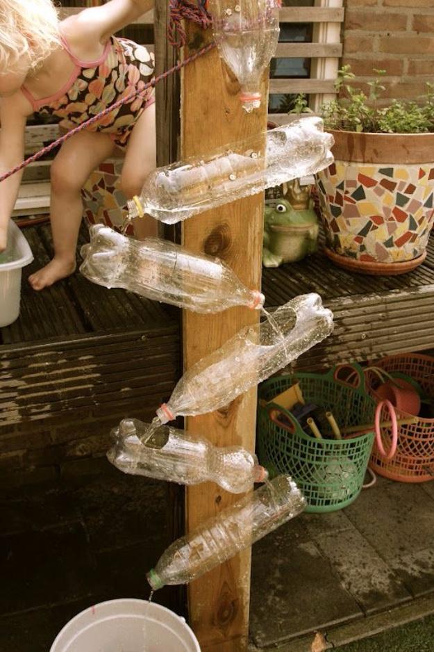 Water wall of clear plastic bottles screwed at angles to a wooden post, water cascading down into a bucket in a garden