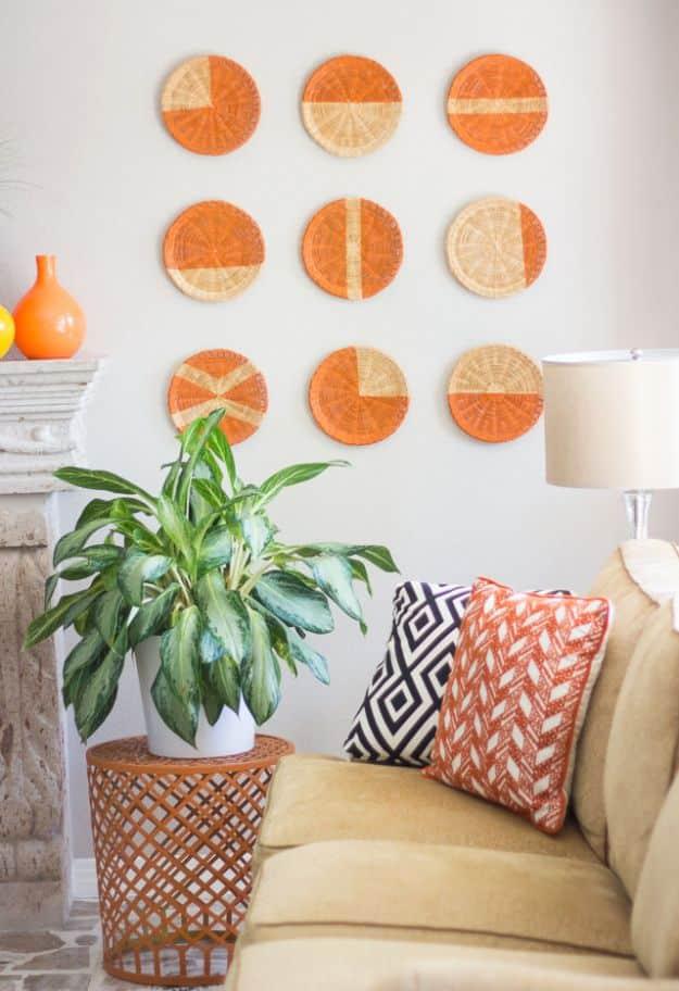 Nine rattan paper plate holders painted with orange citrus segment patterns, hung in a grid above a green plant