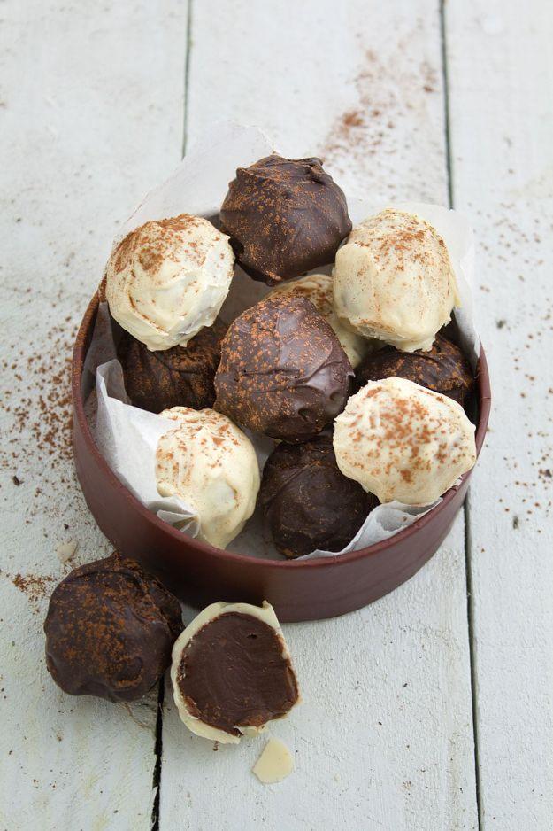 Coffee truffles dusted in cocoa and white chocolate piled in a brown dish, one broken open on white wood