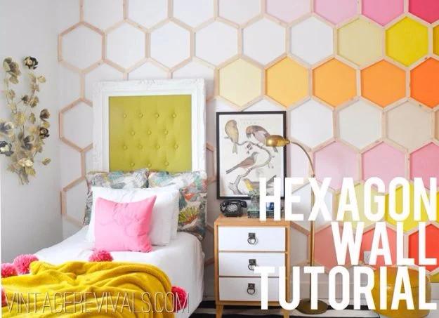 Bedroom wall covered in a large painted wood hexagon honeycomb pattern in pink, yellow and orange behind a white bed