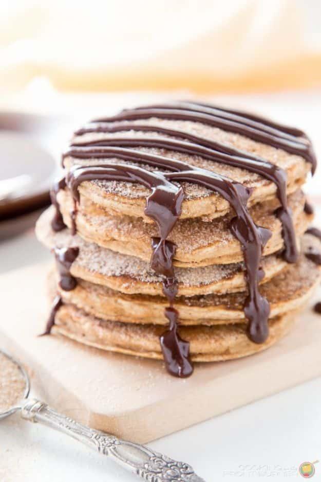 Churro pancakes stacked and dusted with cinnamon sugar, drizzled with dark spicy chocolate sauce on a board