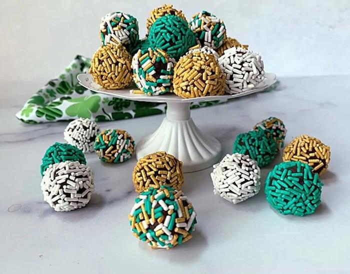 Bailey's Irish cream truffles rolled in green, gold and white sprinkles, on a white cake stand and a marble top