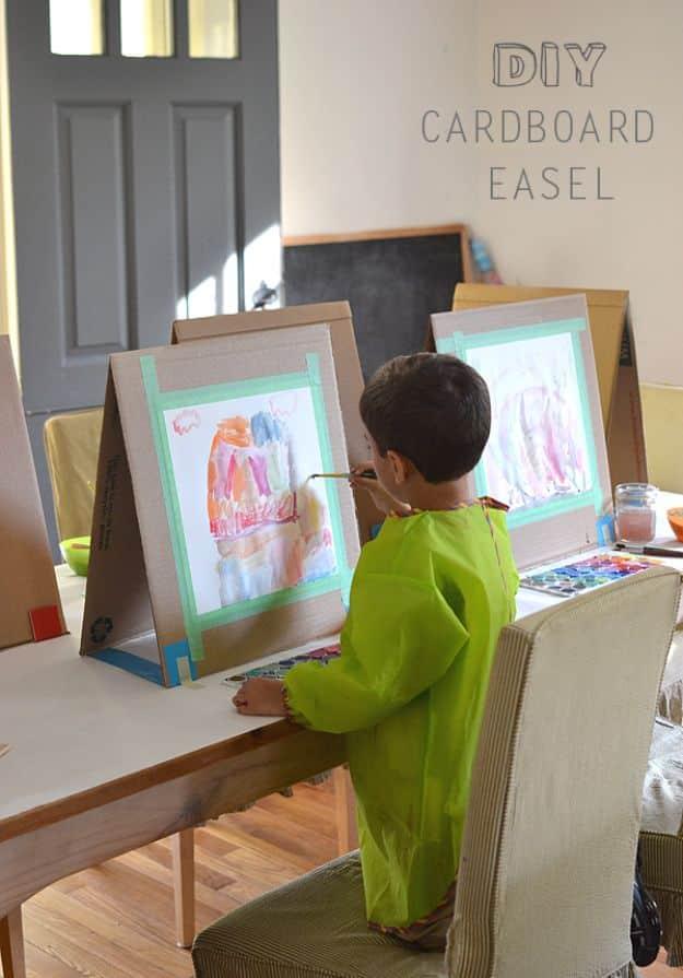 Cardboard craft A frame easel standing on a table, with a child seen from behind in green painting at it