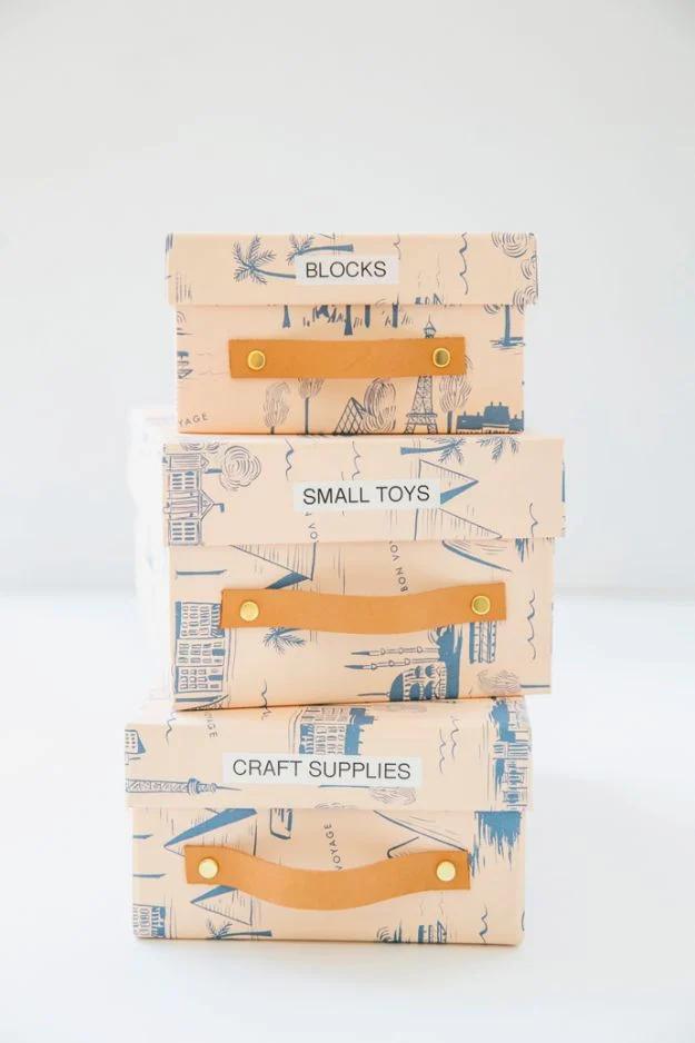 Three shoe boxes covered in patterned paper with leather strap pulls, labeled blocks, small toys and craft supplies