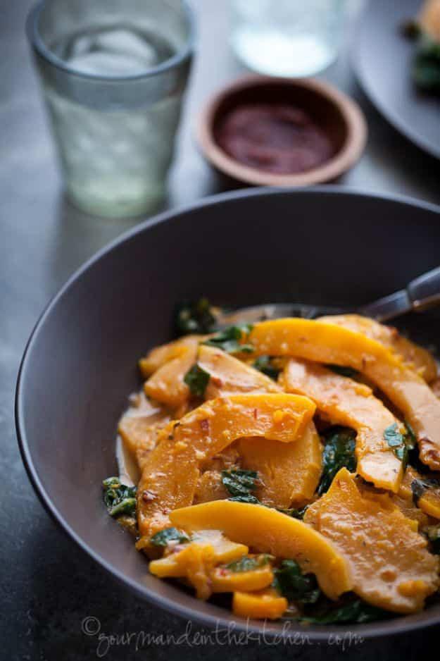 Thai butternut squash and chard curry in coconut milk in a dark bowl with a metal spoon resting inside it